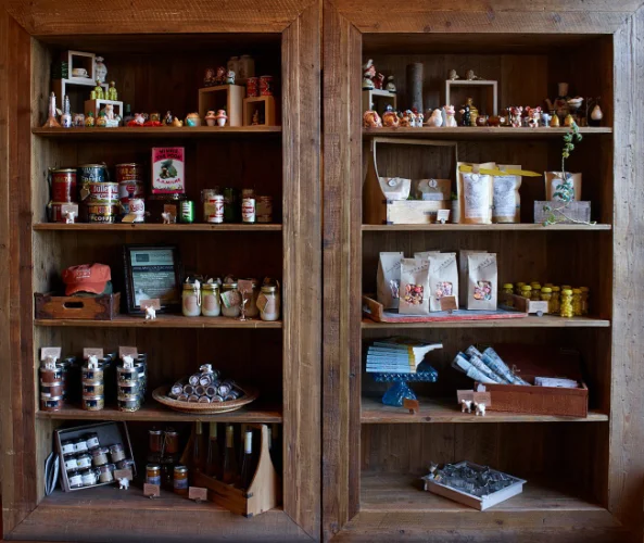 Two wooden shelves in this Summerlin restaurant display assorted items like canned goods, glass jars, packaged food, figurines, bottles, and small decorative objects—all organized neatly on each shelf.